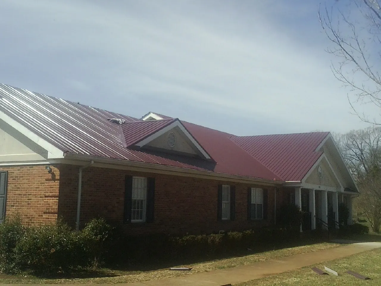 Red metal roof with gabled entries on a long brick building, from a Hail Damage Roof Repair job in Marcus Hook