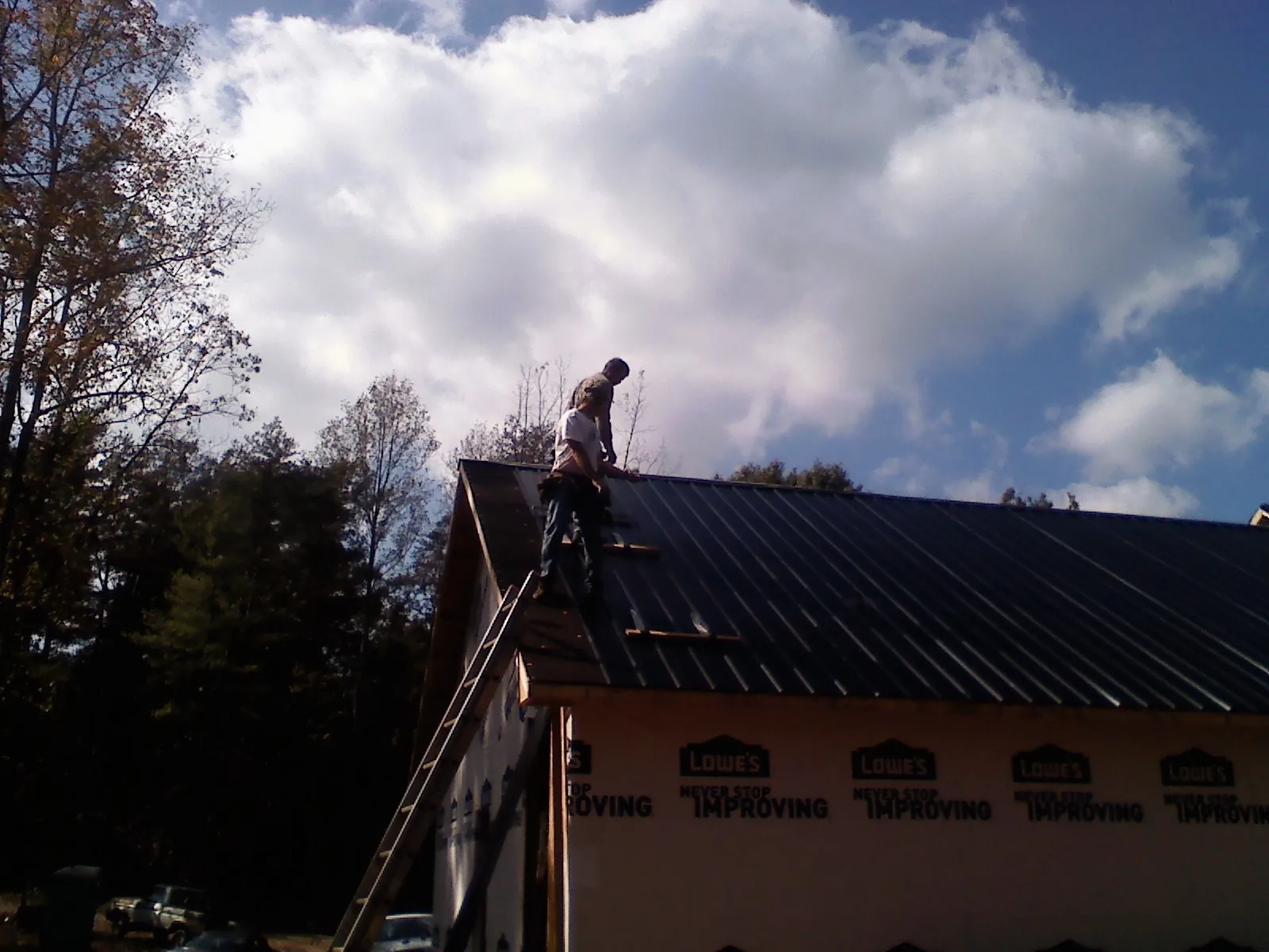 Roofer fastening dark metal panels high against a cloudy sky, from a Roof Inspection job in Marcus Hook
