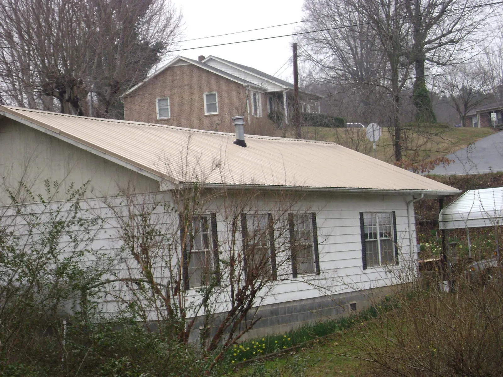 Tan metal roof on a white sided house set into a hillside — Commercial Roofing by Roofing Brothers in Marcus Hook
